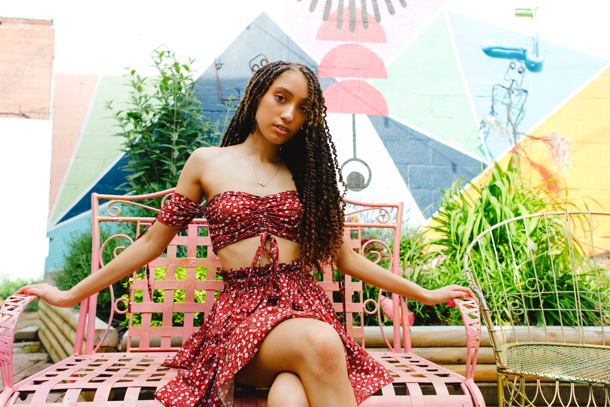 Alize sits in her two piece set on a pink bench in front of a mural