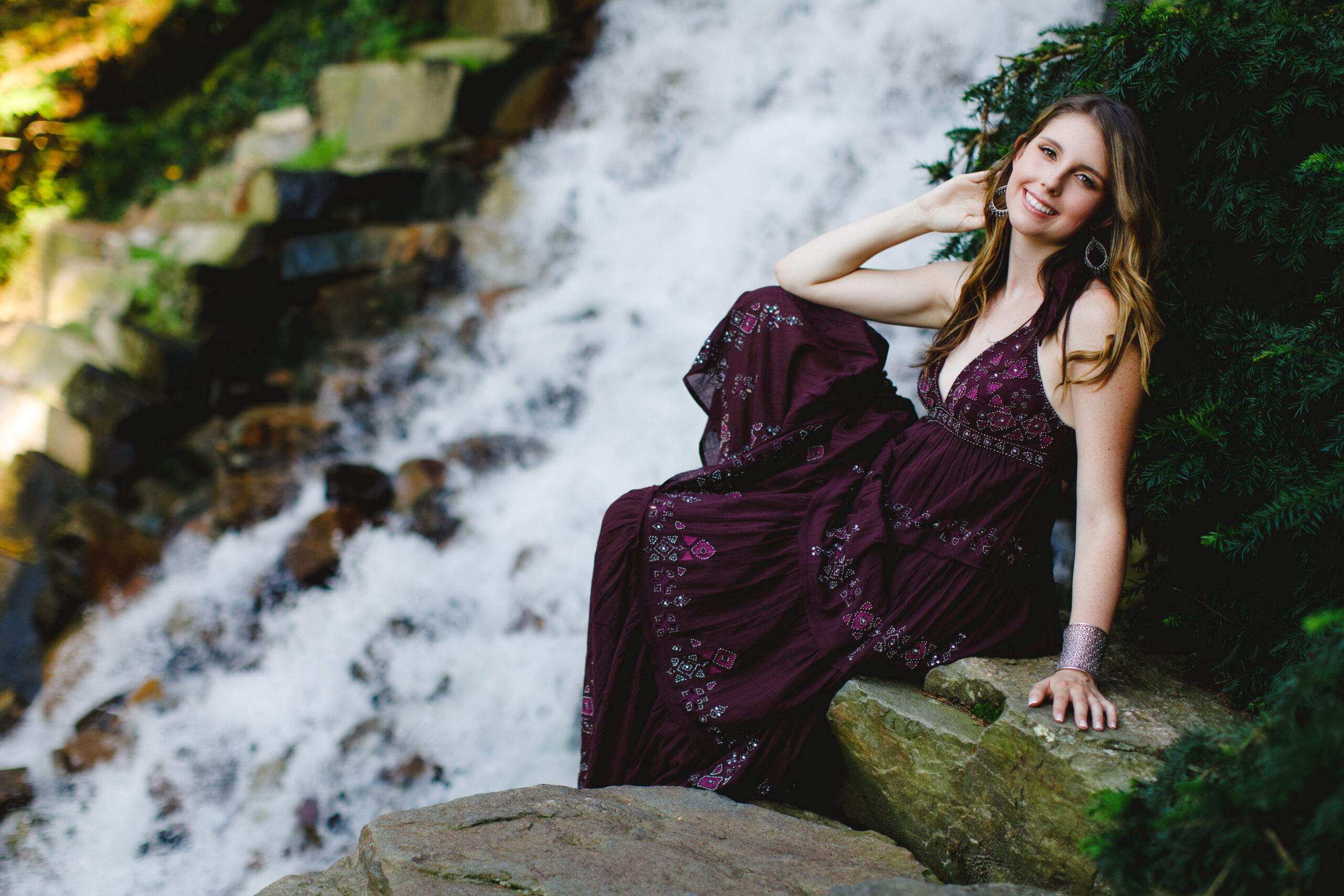Clare poses seated on a mossy rock with a roaring waterfall in the background at Longwood gardens.