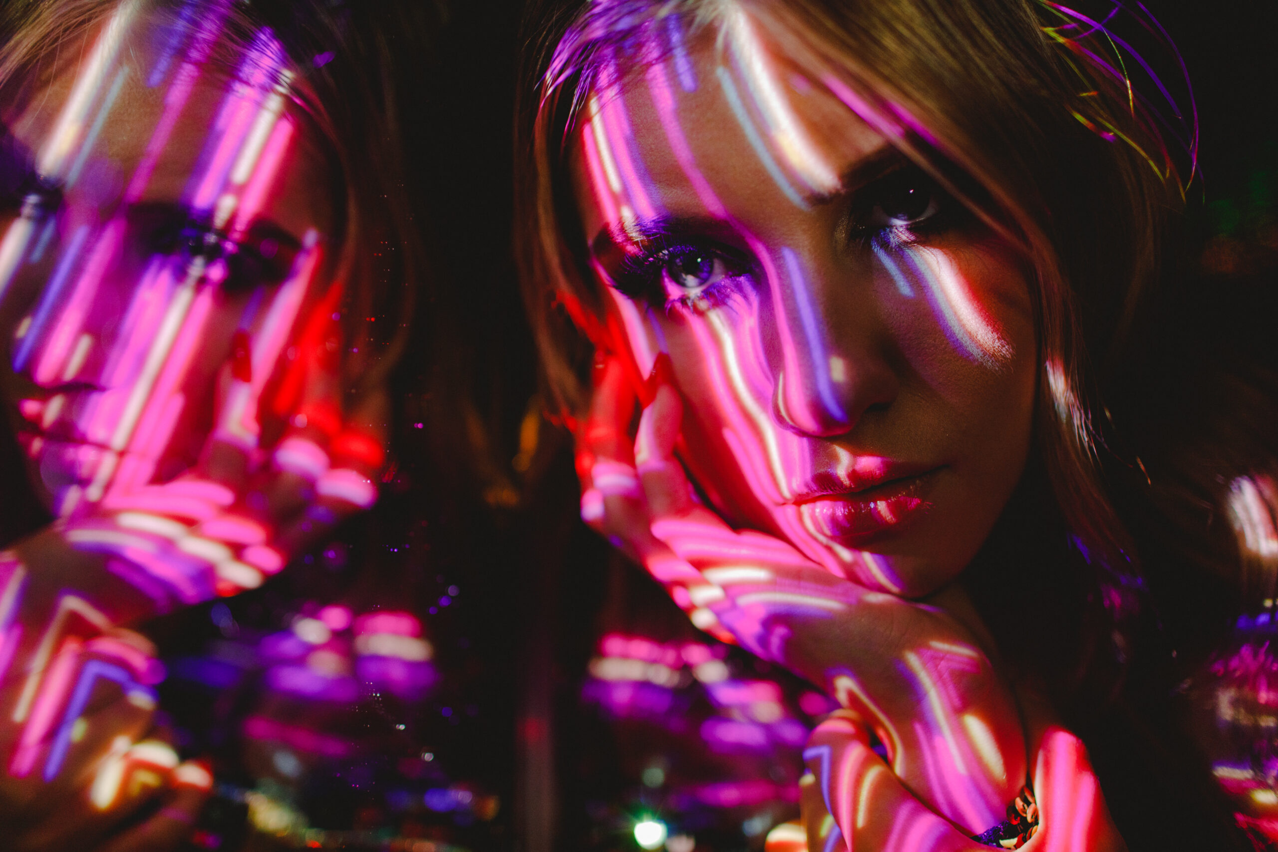 Andrina bathed in neon light beams in her senior editorial photoshoot headshot.