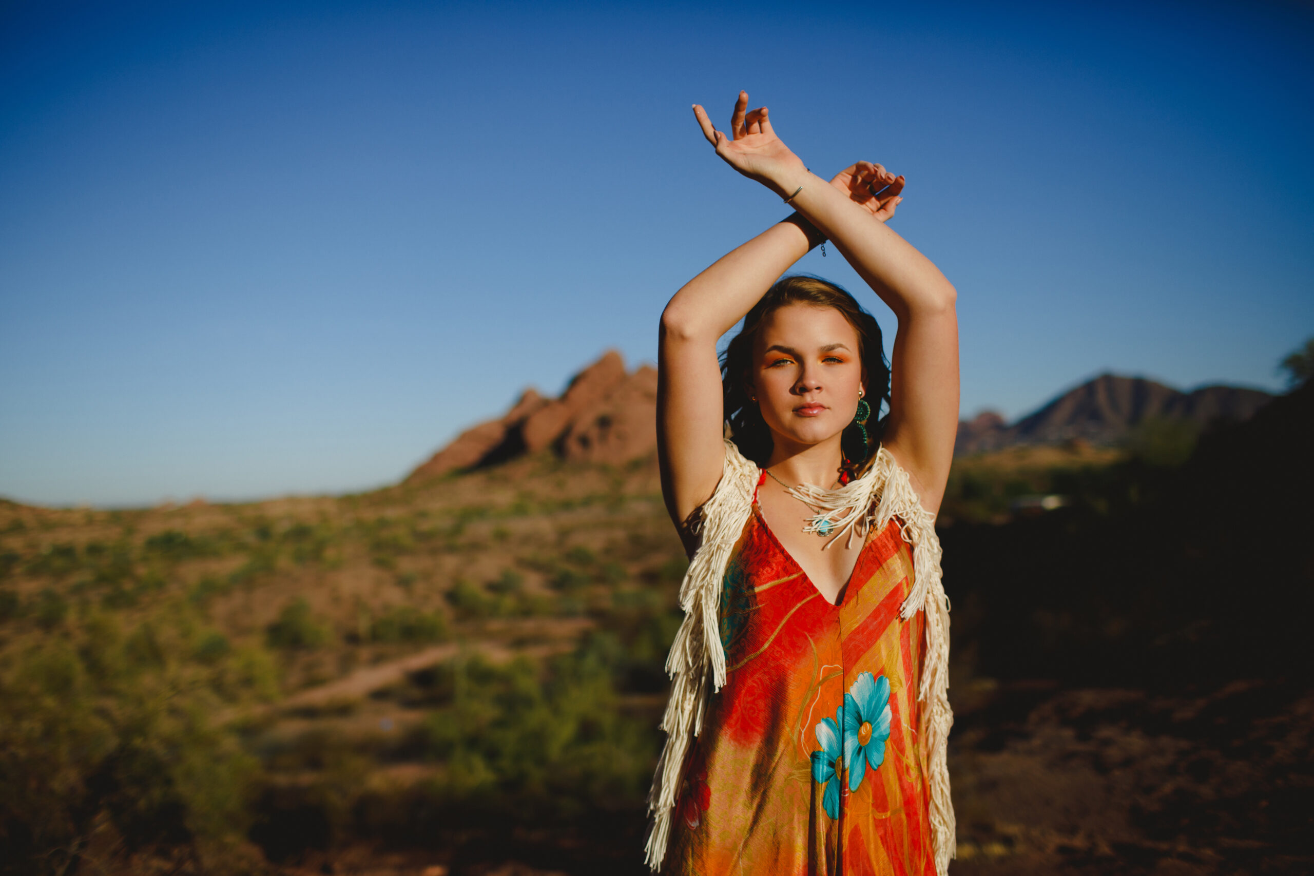 Abby posing in a bright colored jumpsuit and white macrame duster in the desert on location with slice of lime.