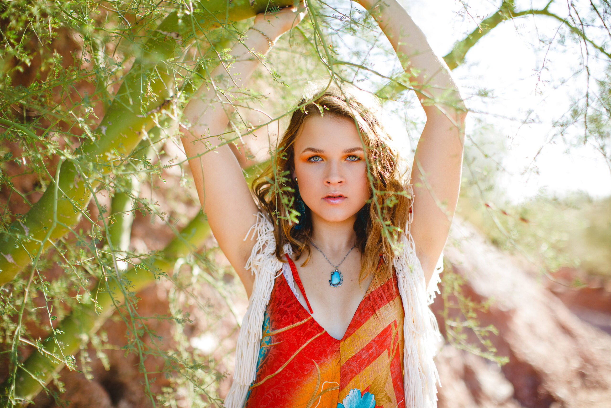 Abby posing in a bright colored jumpsuit and white macrame duster in the desert foliage with slice of lime.