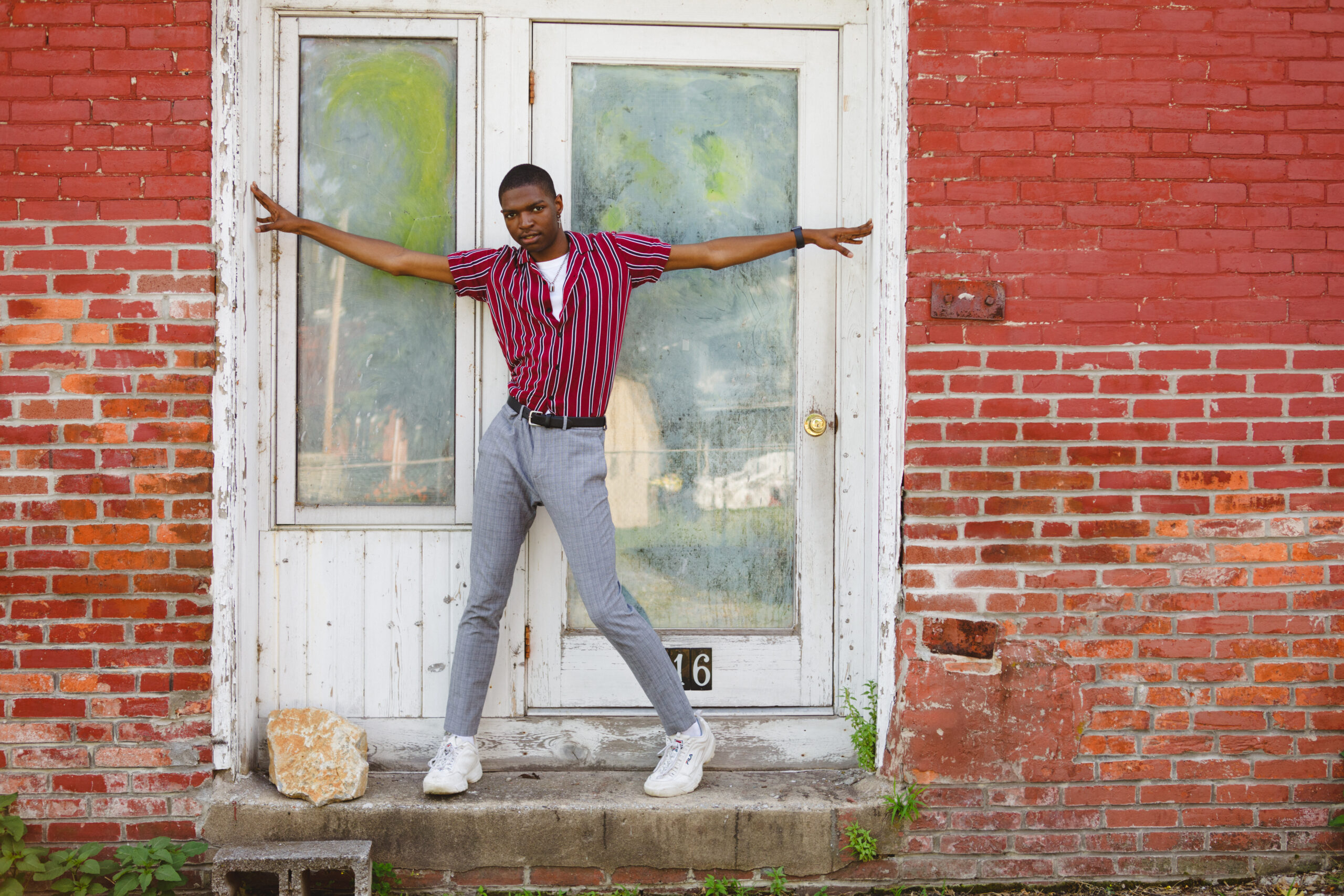 Akiva models in front of a red brick wall in a trendy striped button down top for his senior boy photo shoot.