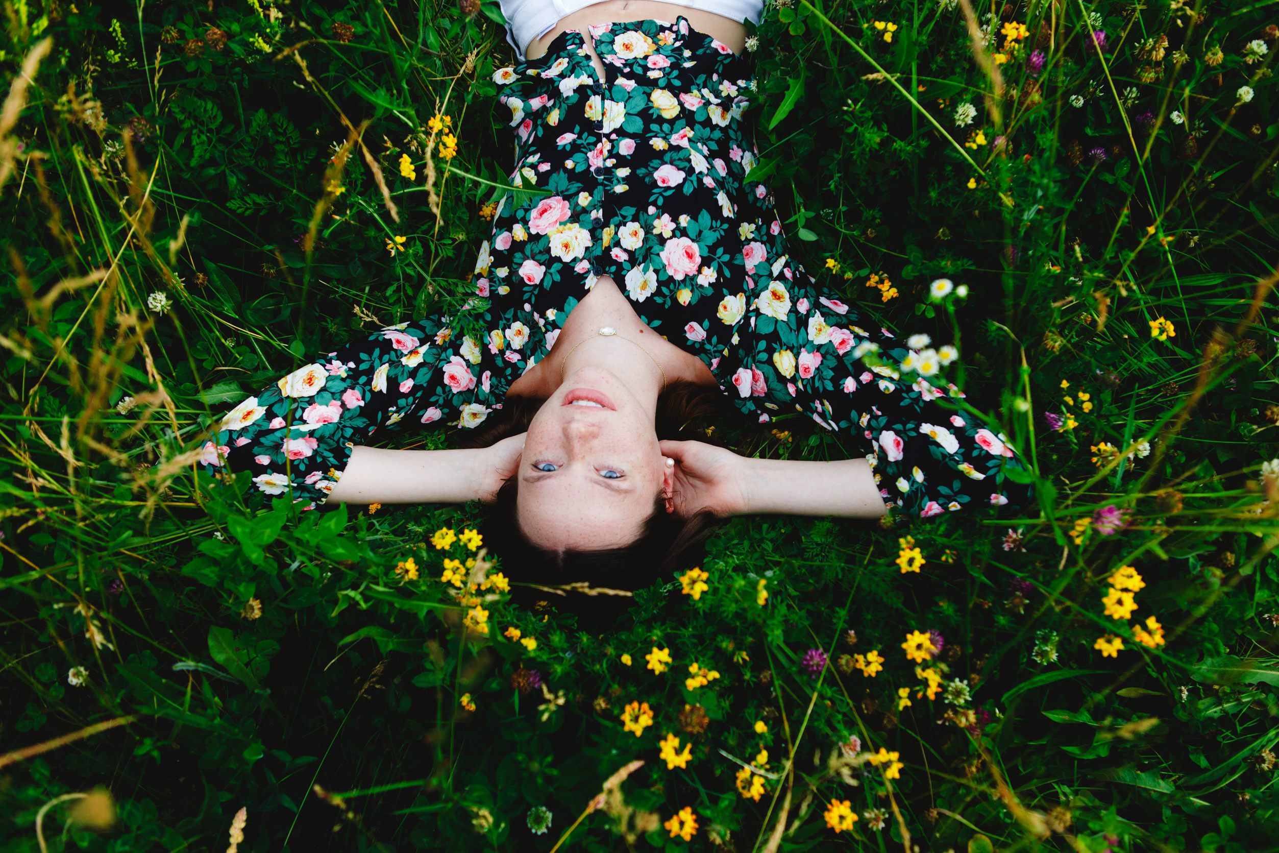 Brunette girl in a floral top laying in a field of flowers