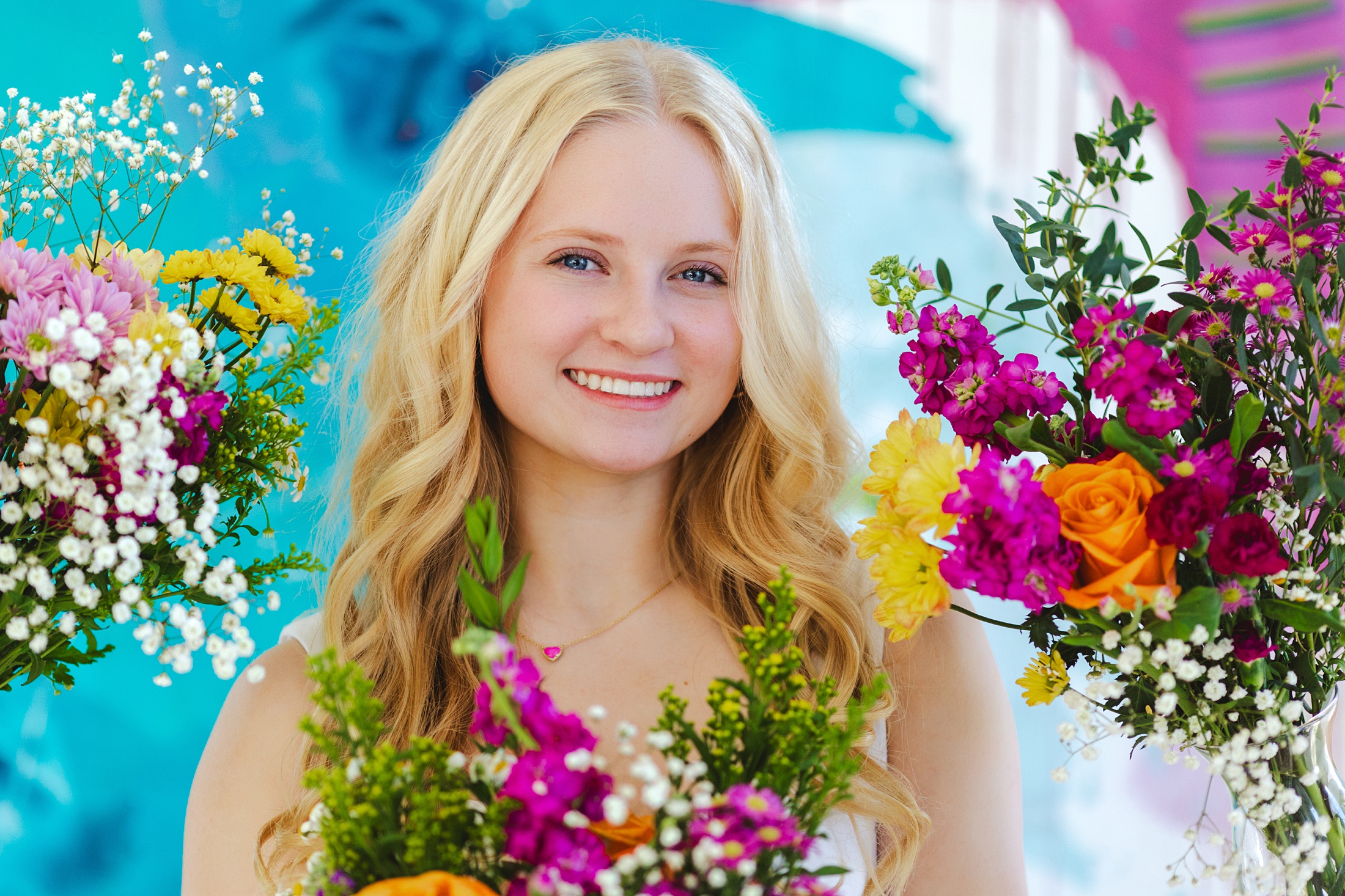 Blonde teengager posing in front of a bold bright canvas painting, with hr face framed by bouquets of flowers at slice of lime photography. 
