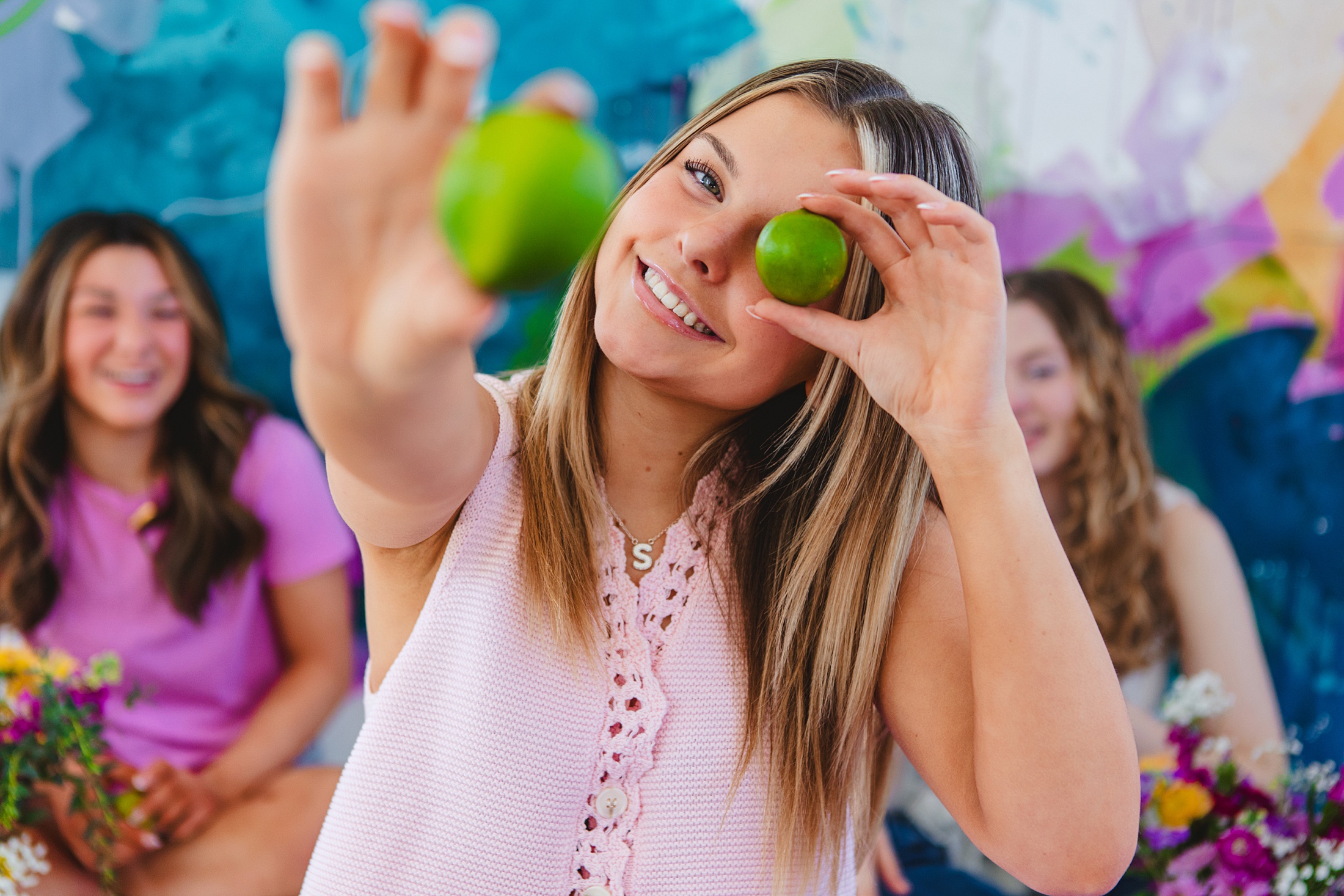 Blonde teenager using limes to be silly and funny against a colorful mural backdrop by Pamela Black Art at the New Cumberland studio of Slice of Lime Photo. 
